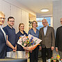 Mehrere Menschen stehen in den neuen Praxisräumen und lächeln in die Kamera. Die Ärztin hat einen Strauß Blumen in der Hand.